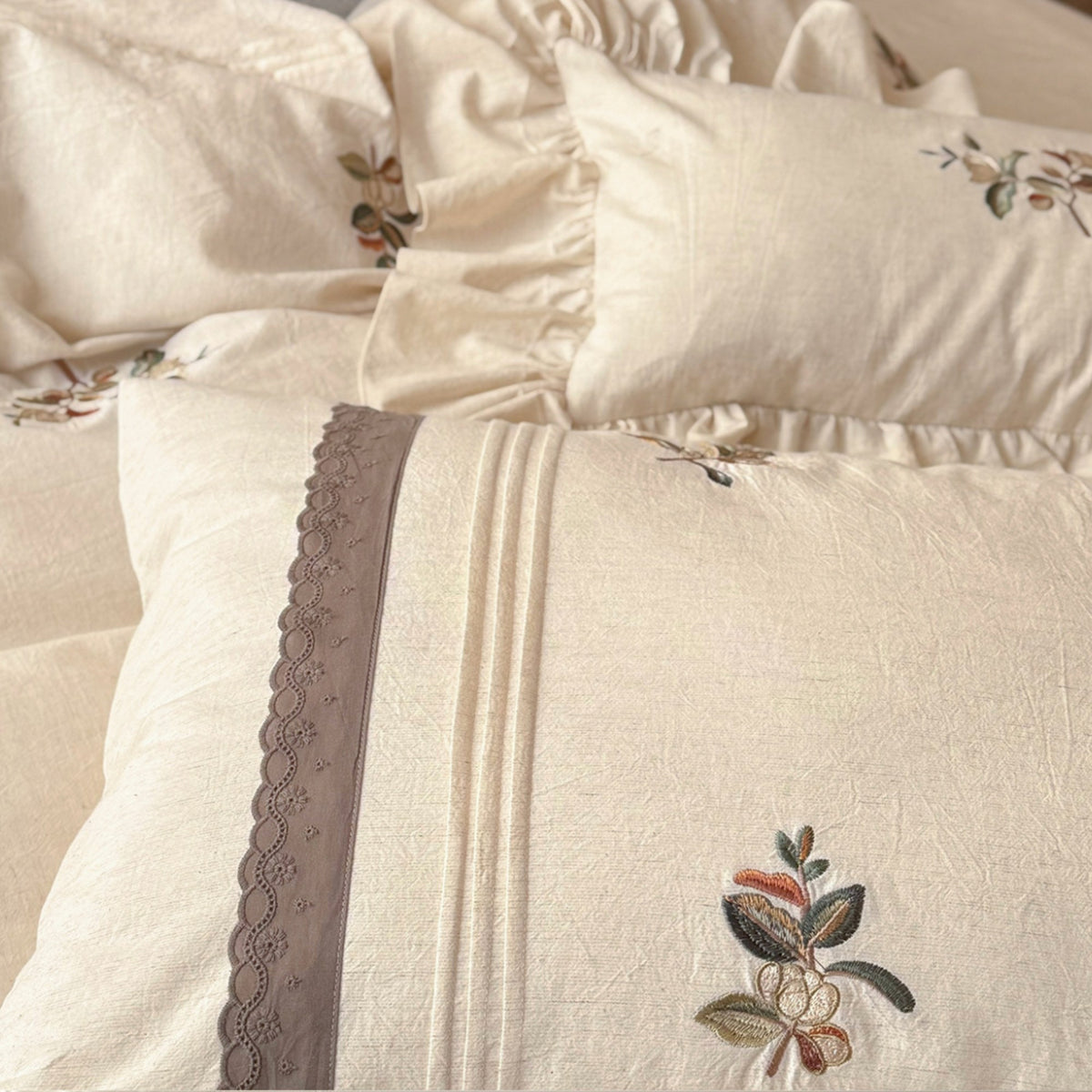 Close-up of a cream-colored bedding set with embroidered floral details and a decorative scalloped trim on the pillowcases.