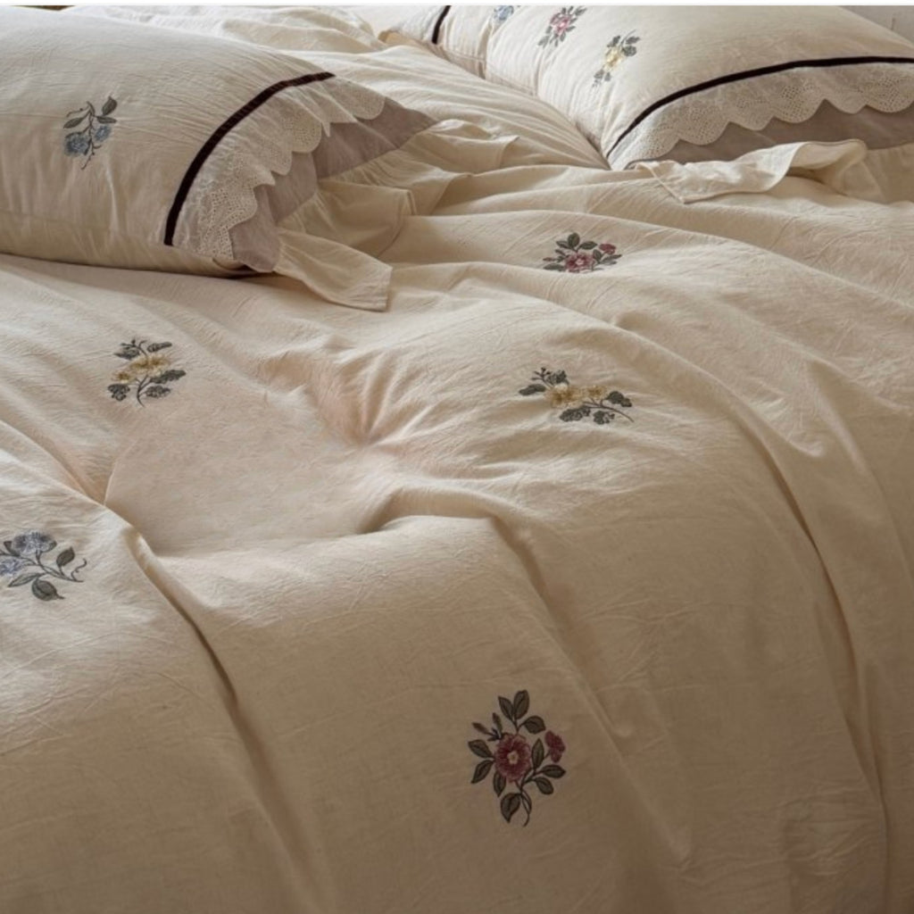 Cream-colored cotton bedding set with embroidered floral motifs and scalloped edges on the pillows.
