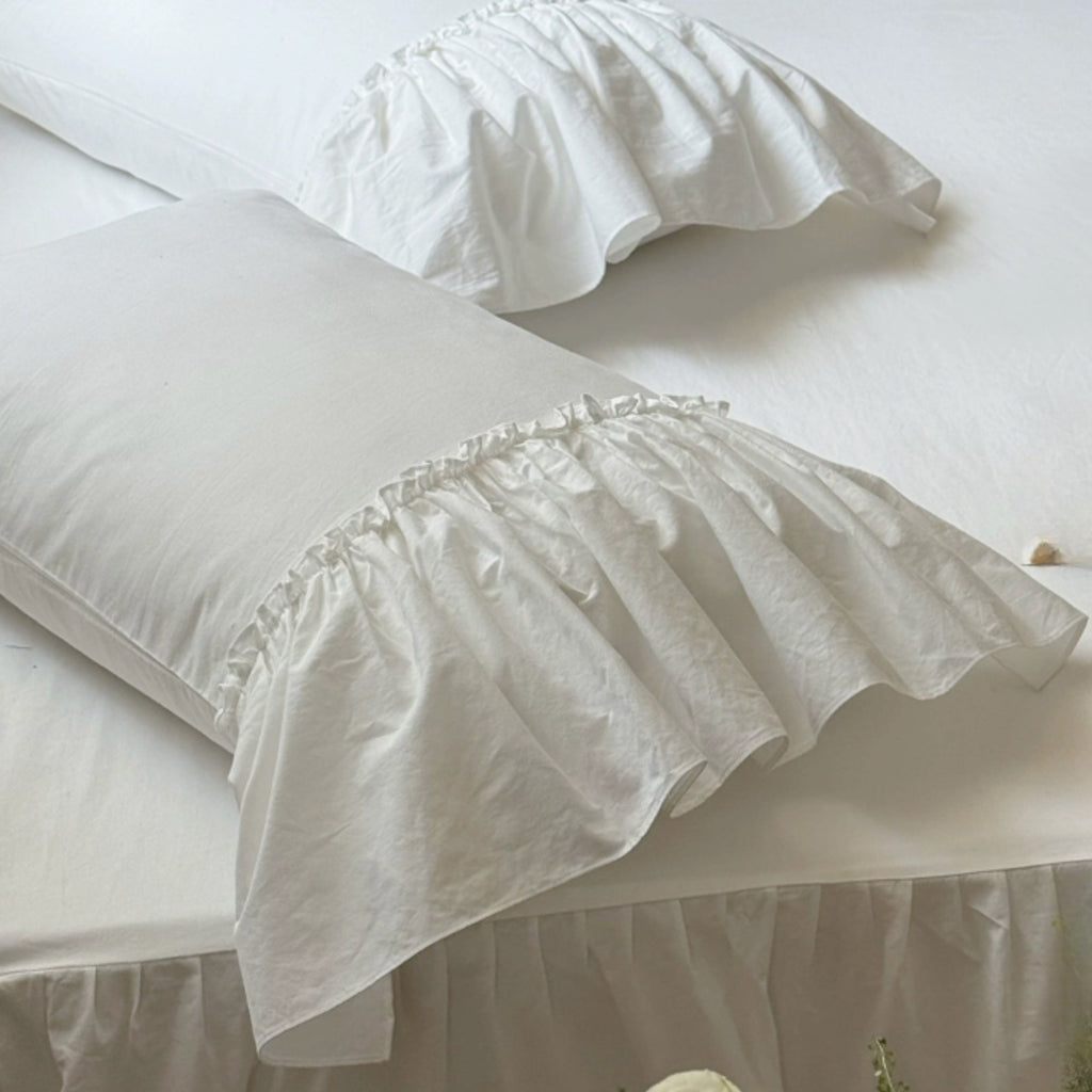 White ruffled pillowcases on a bed with matching white bedding and a white bed skirt.