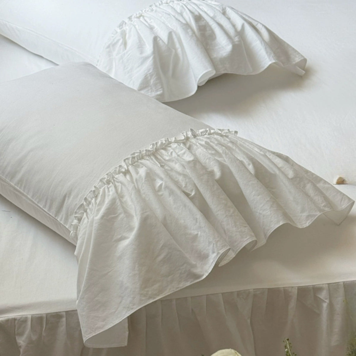 White ruffled pillowcases on a bed with matching white bedding and a white bed skirt.