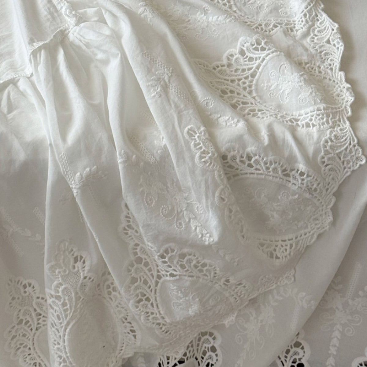 White eyelet lace fabric with delicate embroidered floral patterns and scalloped edges, draped to show texture and pattern details.