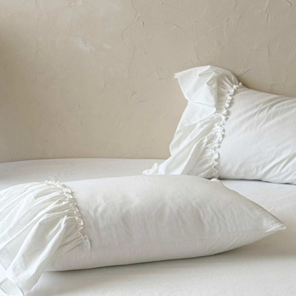 White ruffled pillowcases on a bed against a textured beige wall.