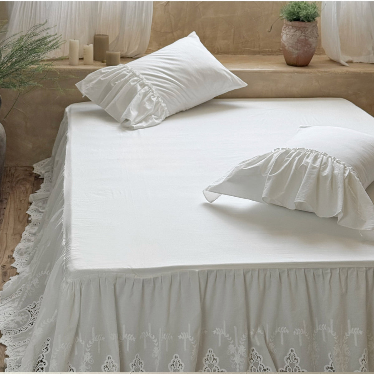 A white bedspread with a matching ruffled pillowcase and a lace-trimmed bed skirt, styled in a warm, rustic bedroom setting.