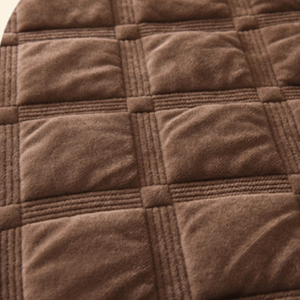 A close-up of a brown quilted fabric with a grid pattern of square sections and stitched seams.