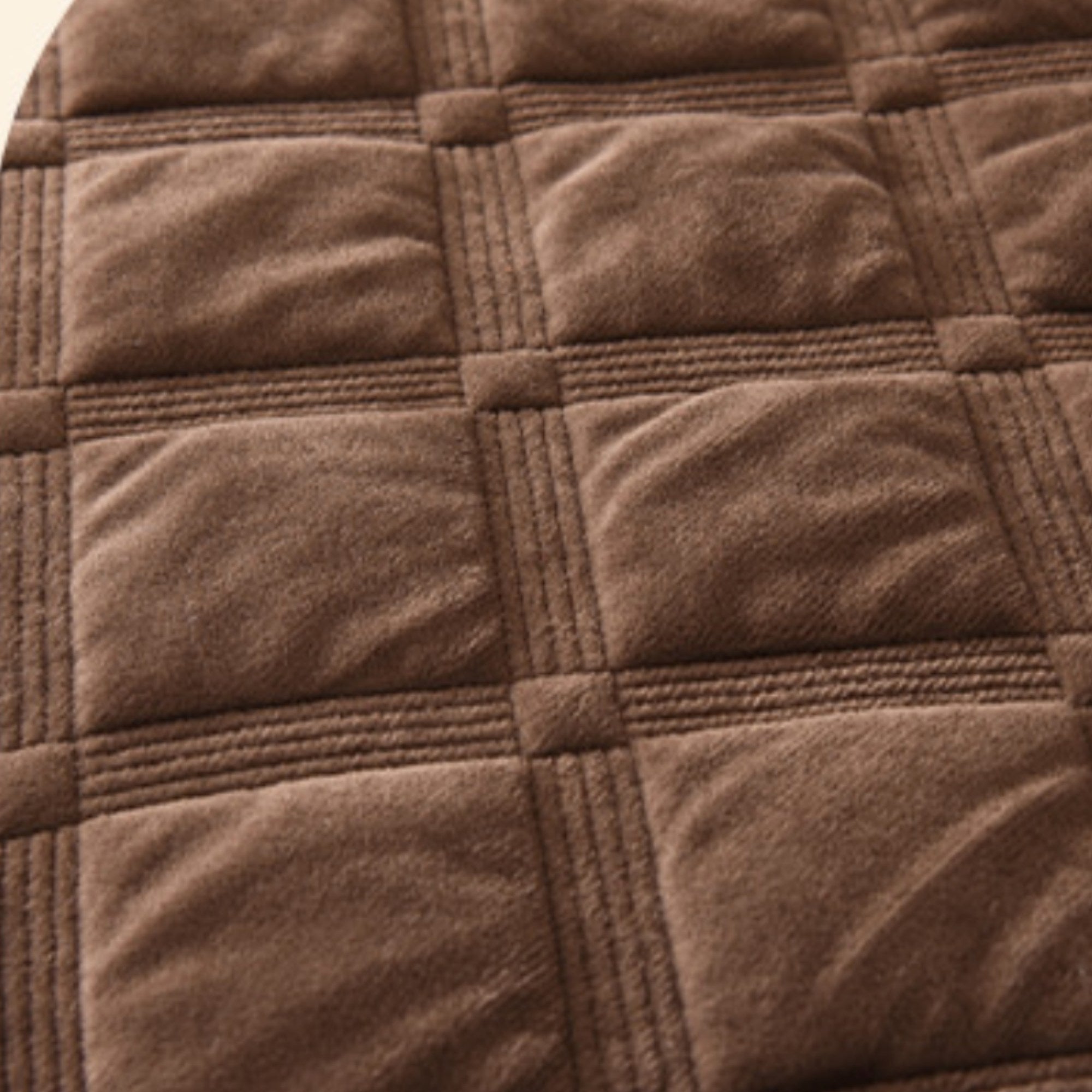 A close-up of a brown quilted fabric with a grid pattern of square sections and stitched seams.