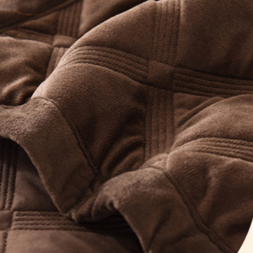 Close-up of a brown plush quilted blanket with stitched panel details and soft folds.