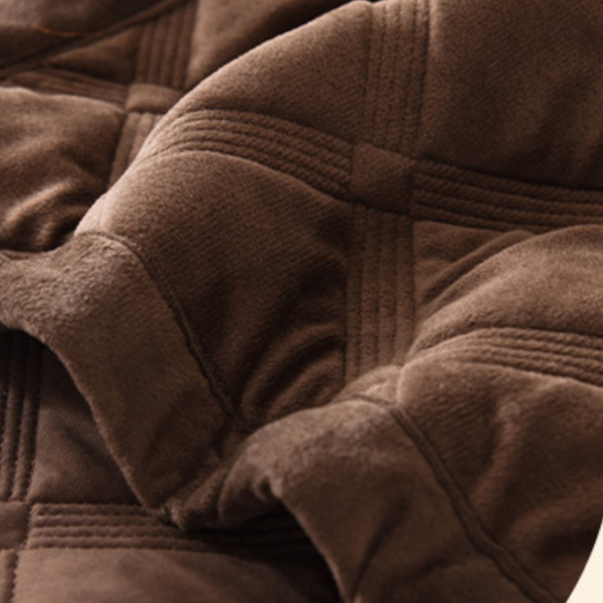 Close-up of a brown plush quilted blanket with stitched panel details and soft folds.