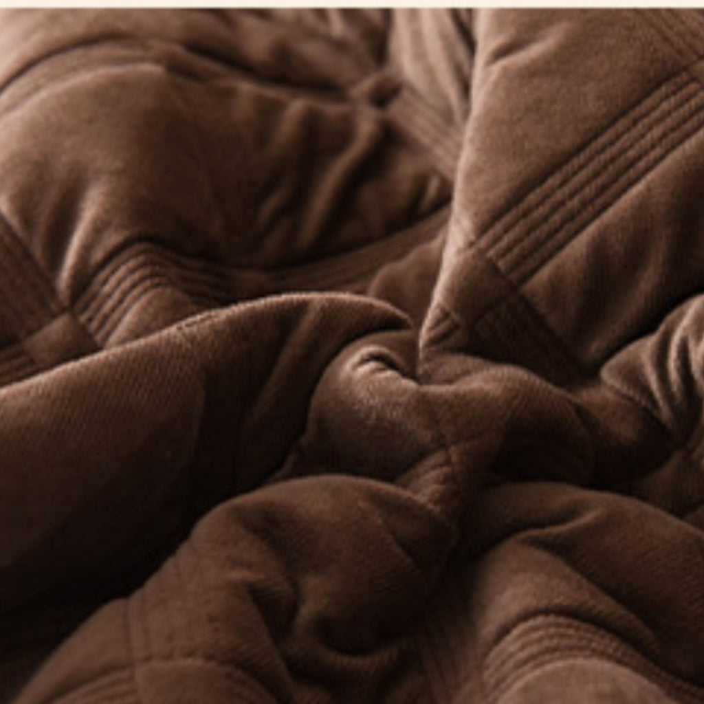 A close-up of a brown quilted blanket with a plush, soft texture and stitched panel details.