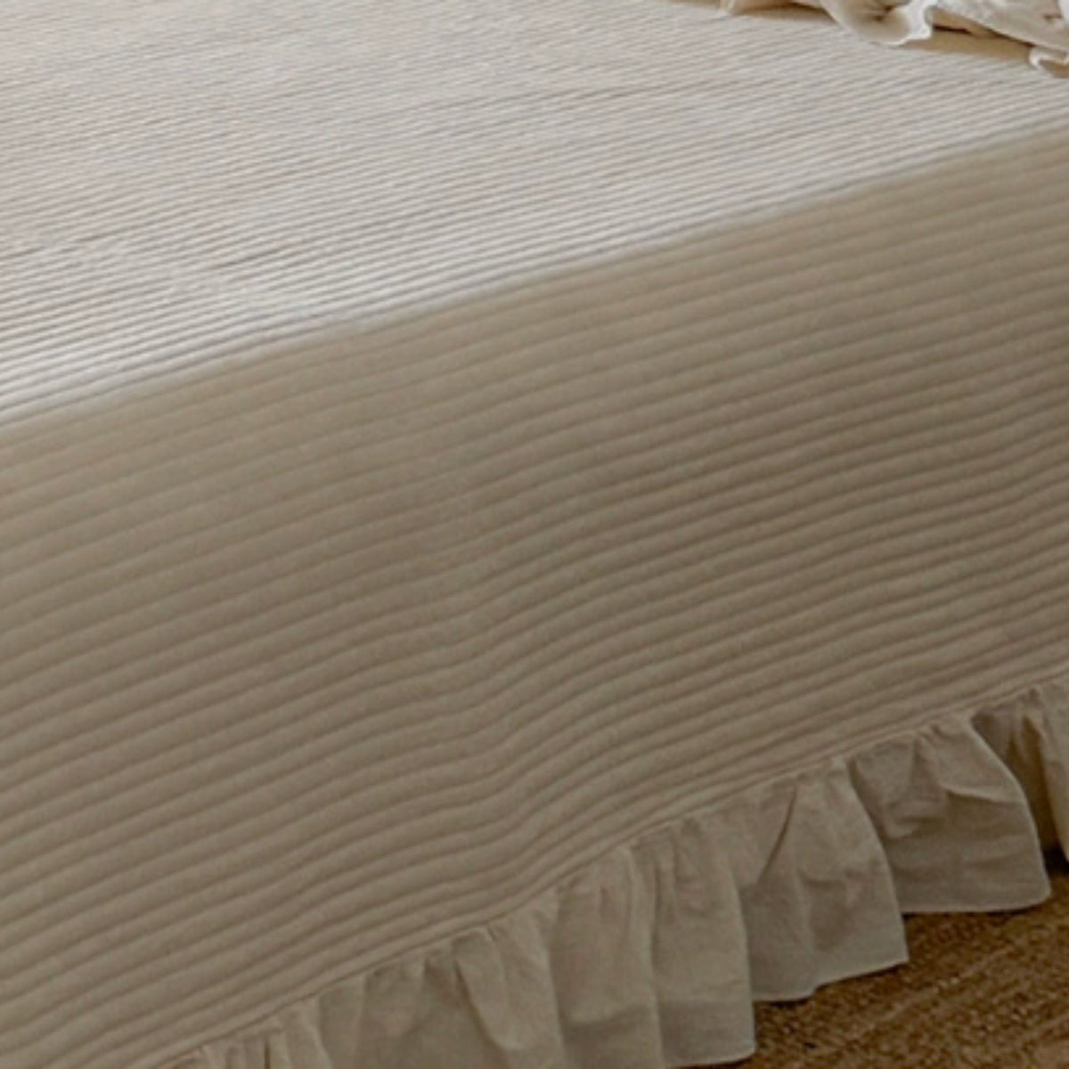A close-up of a cream-colored bedspread or sheet with a ruffled edge, showing a textured horizontal stripe pattern.