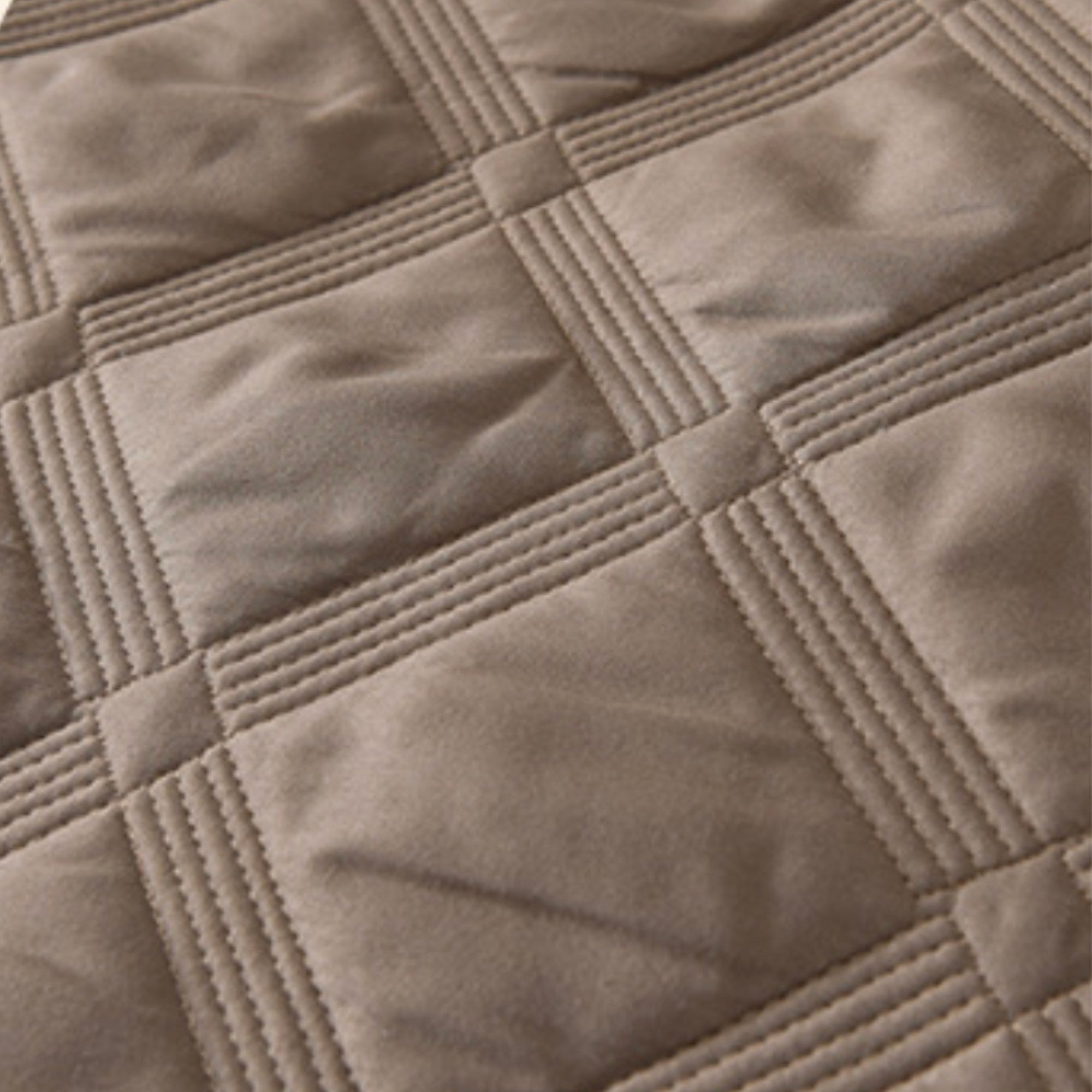 Close-up of a quilted fabric surface in a warm taupe-beige color, showing stitched square panels and stitched border lines.
