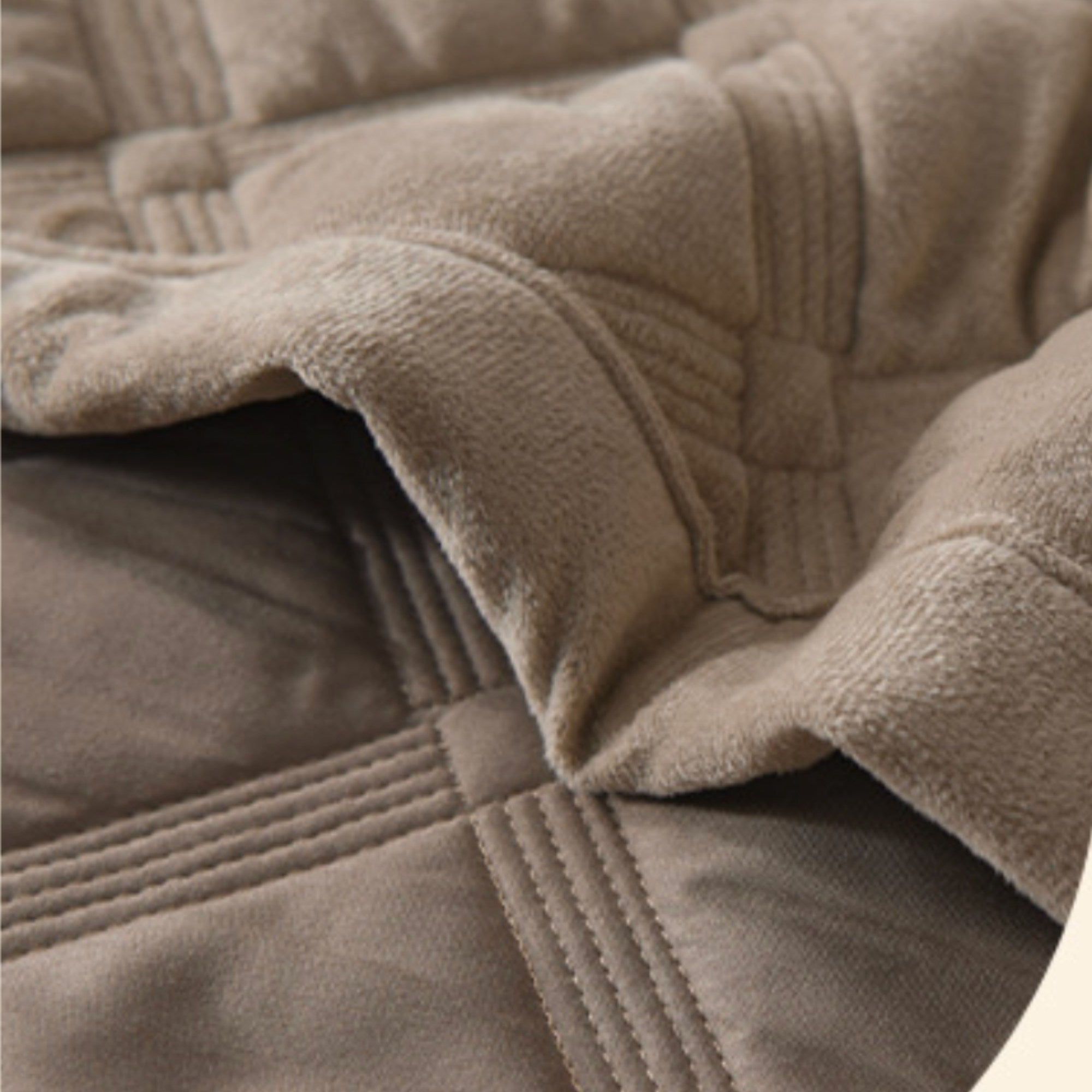 Close-up of a quilted blanket showing a soft taupe-brown sherpa lining and stitched quilted fabric in a matching taupe color.