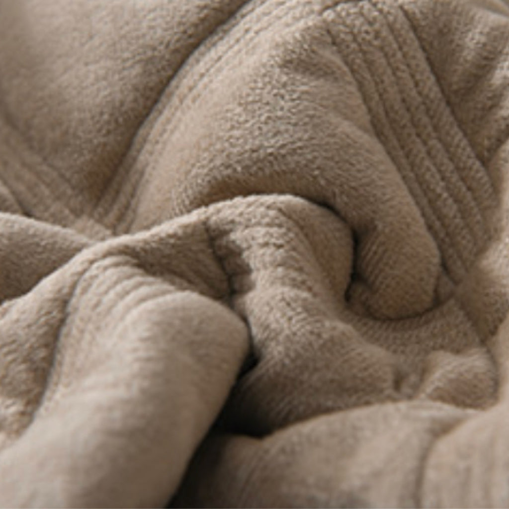 A close-up of a soft, plush fleece blanket in a warm taupe-beige color, showing its textured fabric and folded folds.