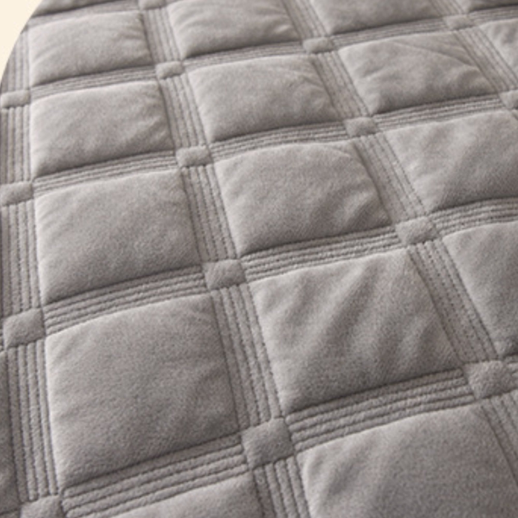 Close-up of a gray quilted fabric surface with stitched square panels and raised seam lines.