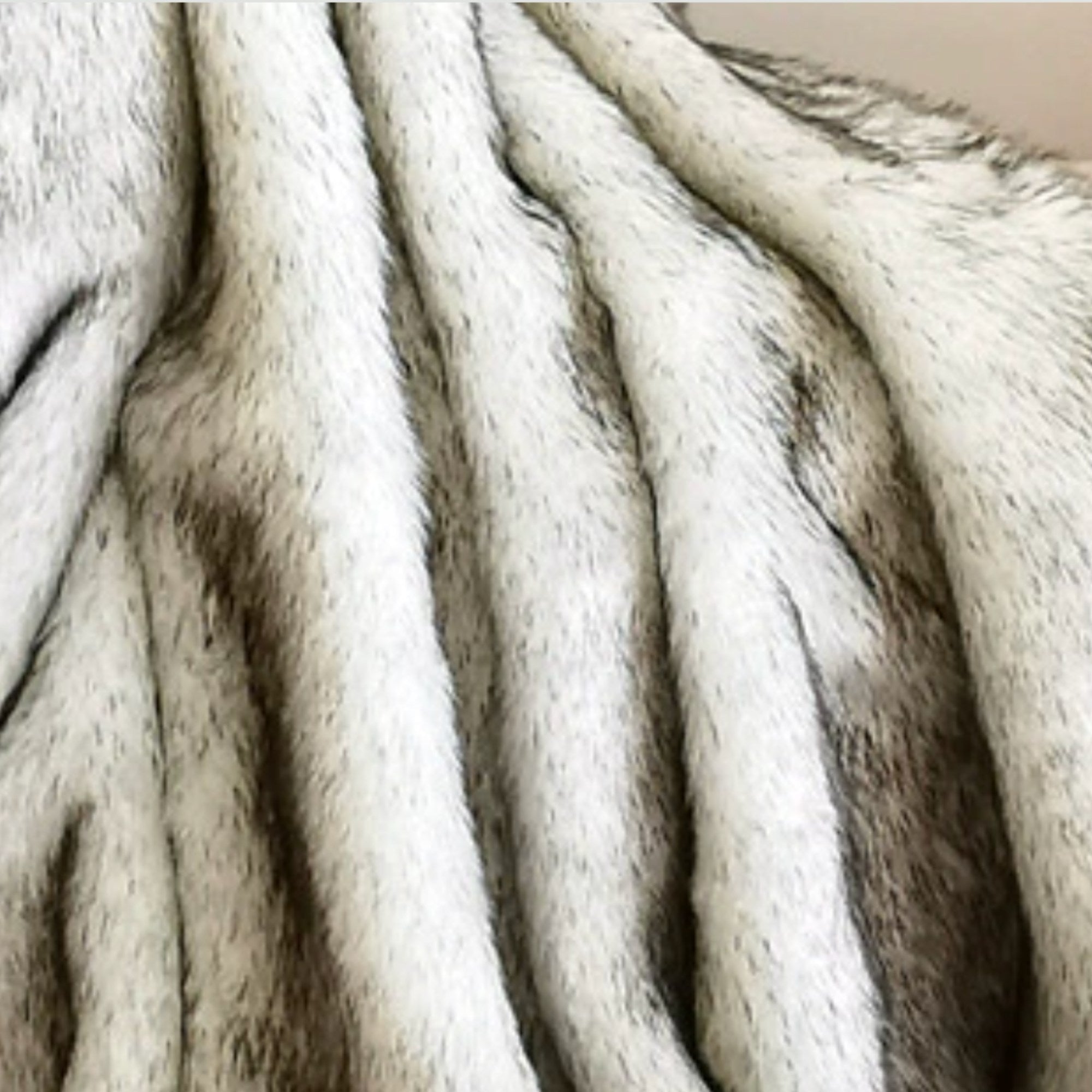Close-up of a faux fur or animal-print textile with vertical folds, showing a mix of off-white, beige, and dark brown tones.