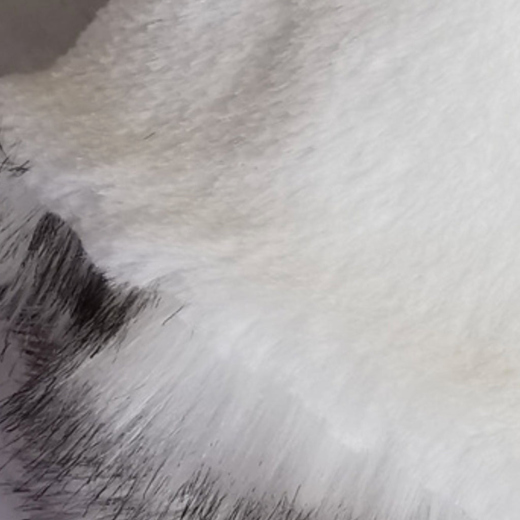 A close-up texture shot of white faux fur fabric with a small section of black fur visible in the lower left corner.