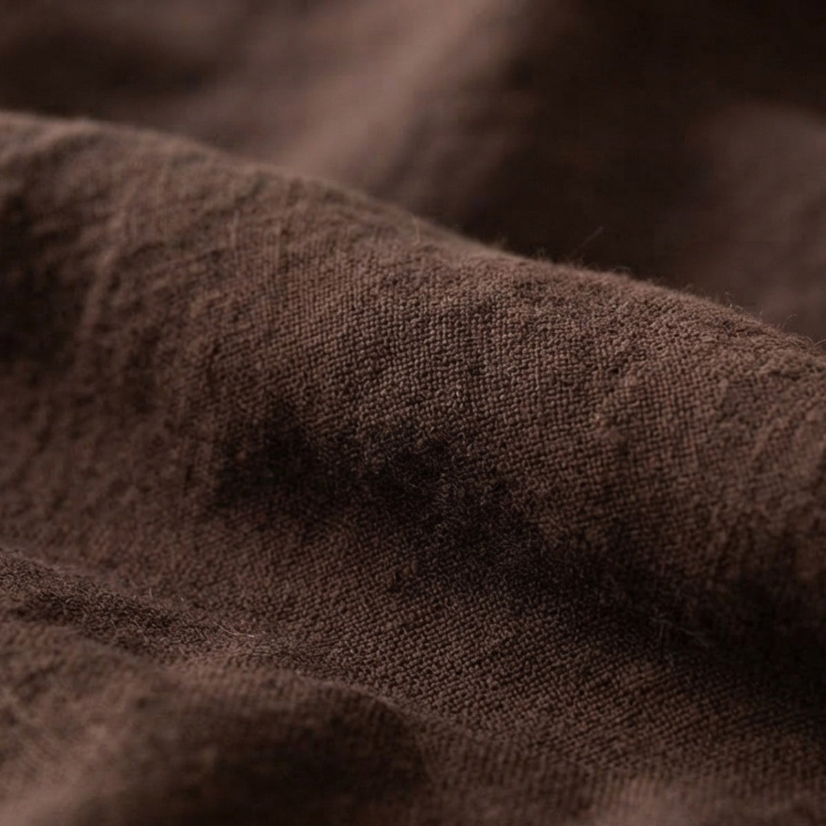 A close-up of draped dark brown fabric with a soft, slightly fuzzy texture and visible weave detail.