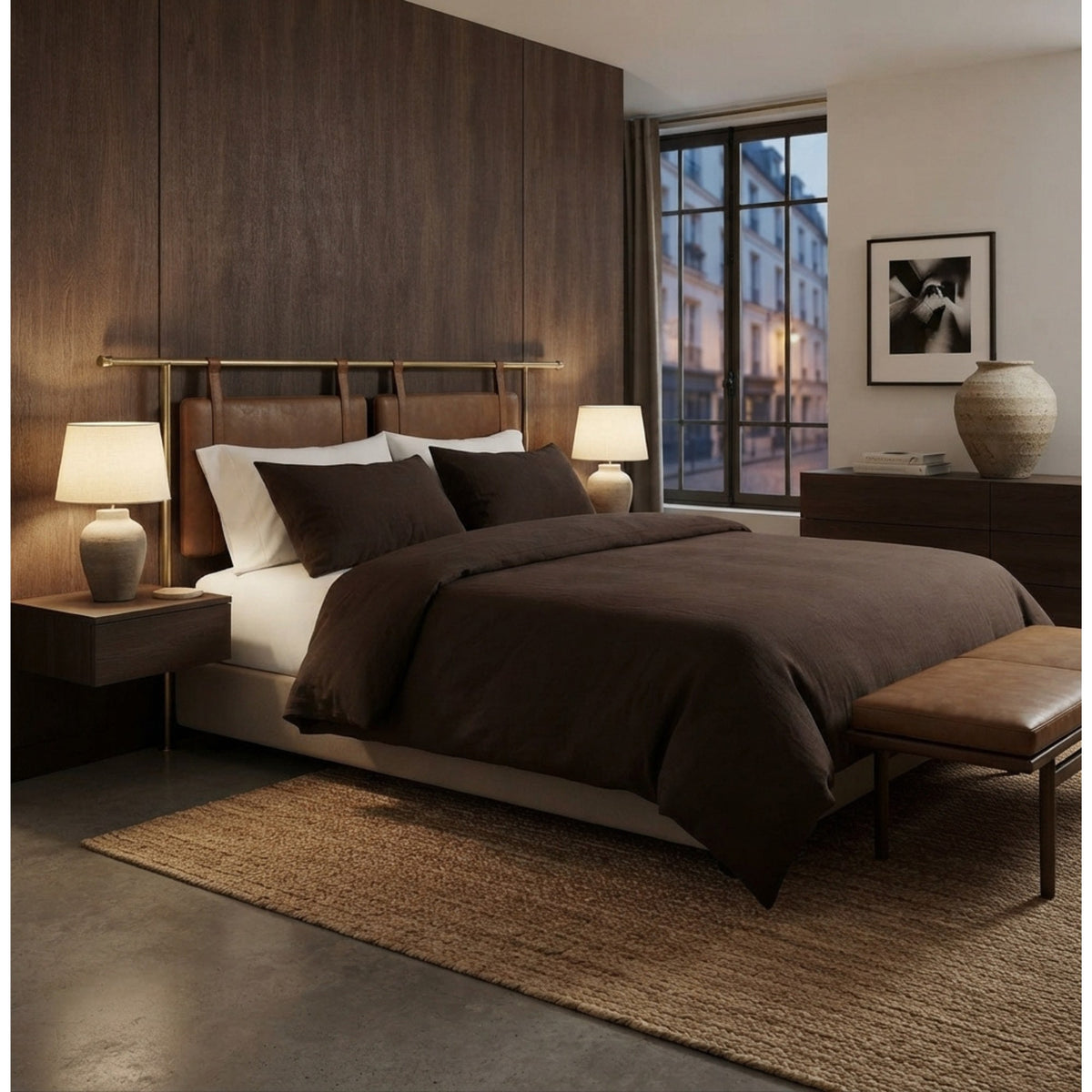 A modern bedroom featuring a bed dressed in dark brown and white bedding, set against a dark wood-paneled wall with matching bedside tables and lamps.