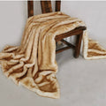 A plush faux-fur style throw blanket in warm beige and tan tones draped over a dark wooden chair against a plain light gray studio background.