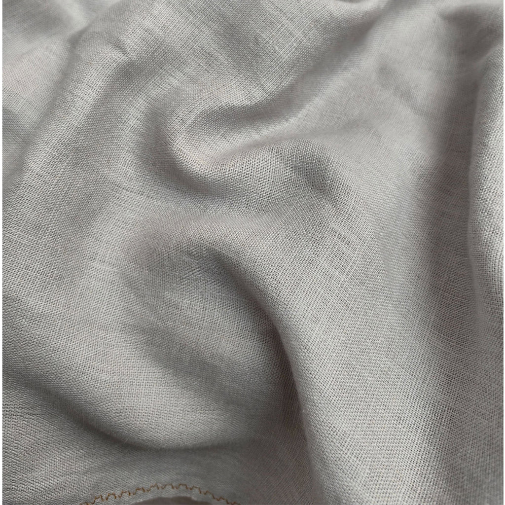 A close-up of draped light gray fabric with a soft woven texture and subtle folds.