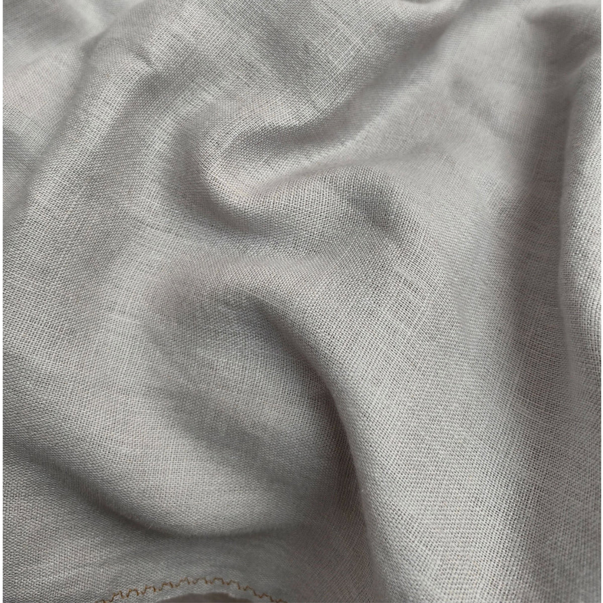 A close-up of draped light gray fabric with a soft woven texture and subtle folds.