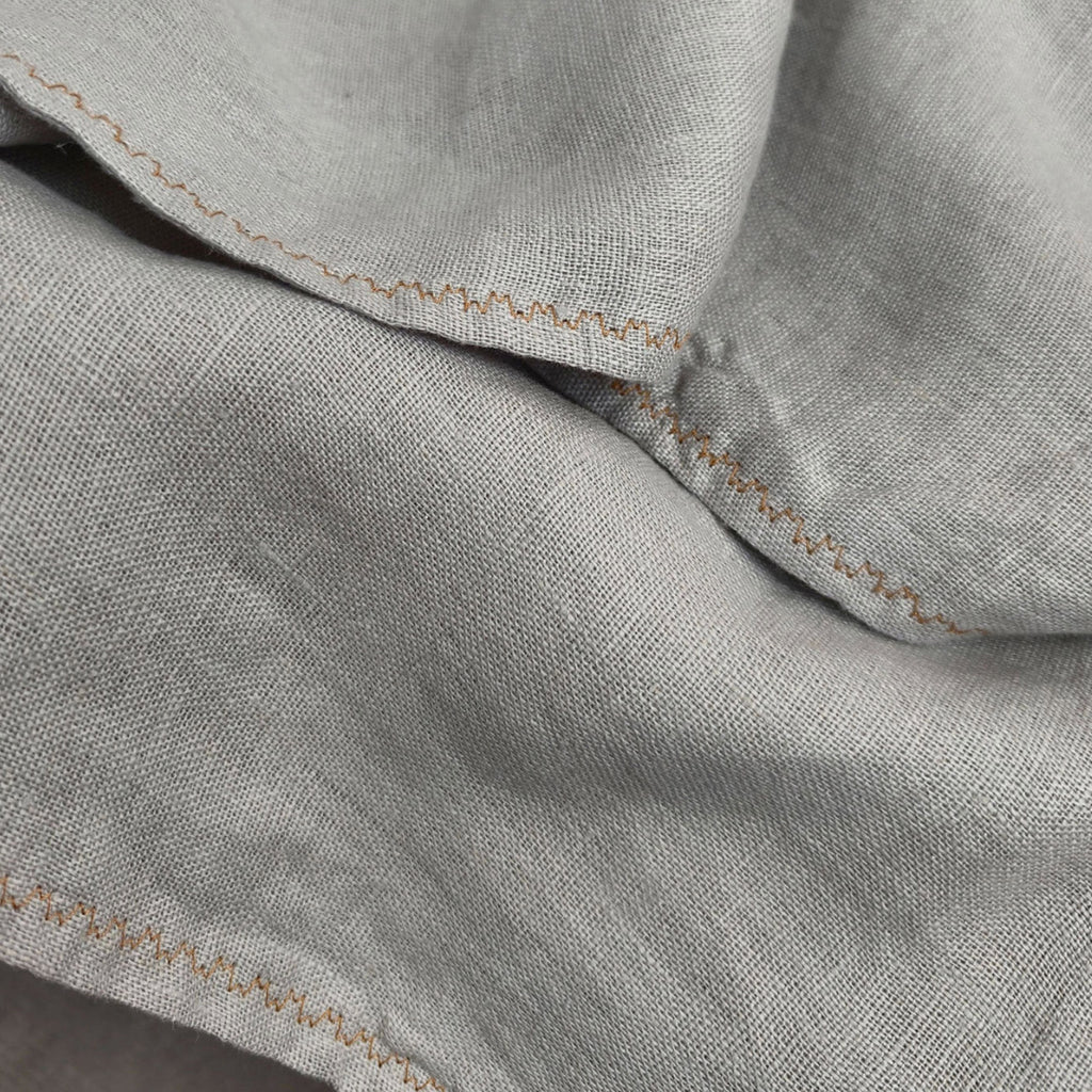 Close-up of a light gray linen fabric with visible texture and tan zigzag stitching along the edges.