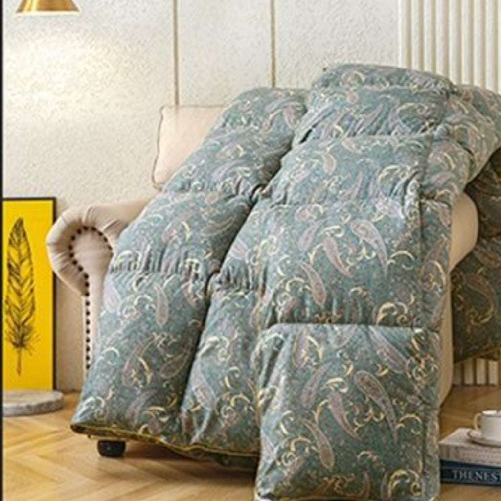 A thick quilted comforter with a blue-green paisley pattern draped over a beige armchair in a living room setting.