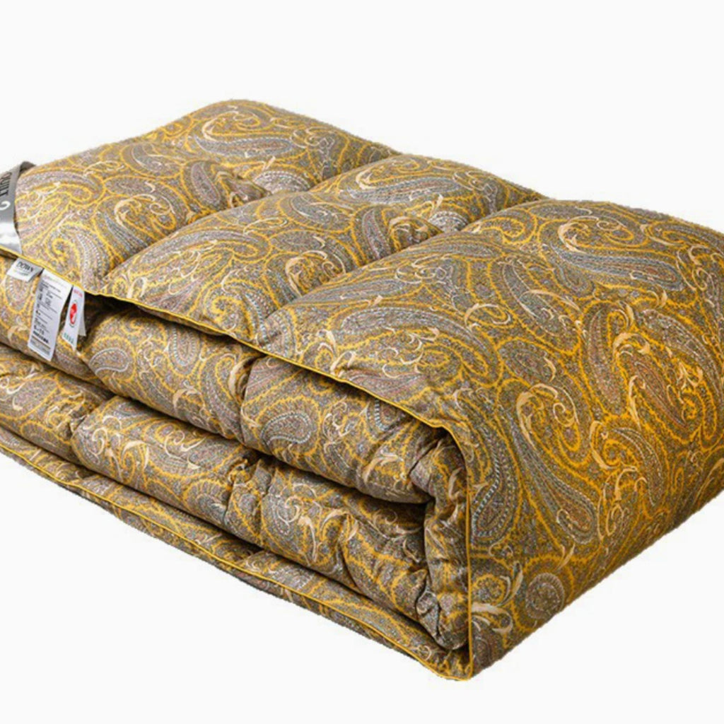 A folded quilted comforter or duvet with a yellow-gold and gray paisley pattern, shown on a plain white background with a product tag attached.