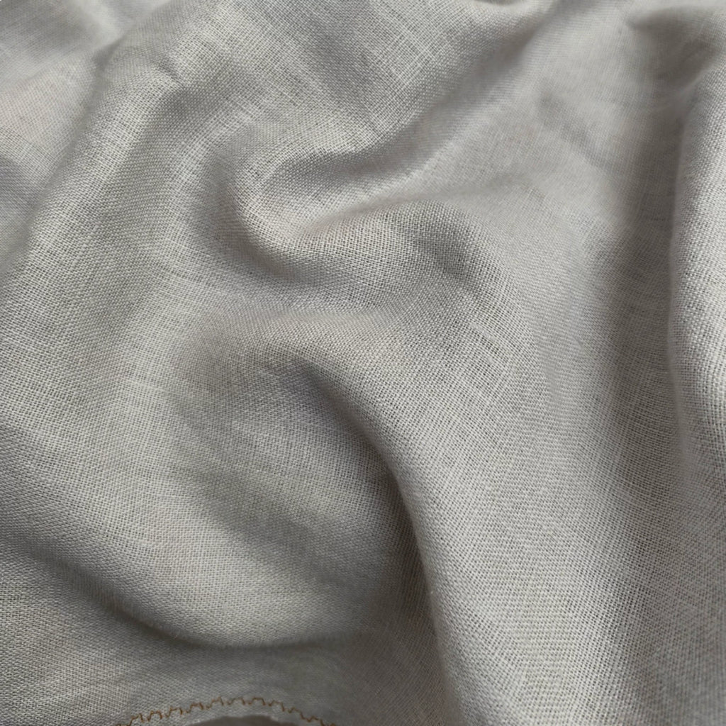 A close-up of draped light gray fabric with a soft woven texture and subtle shadows.