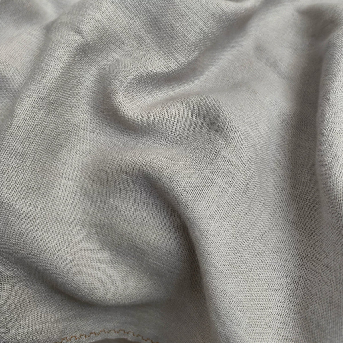 A close-up of draped light gray fabric with a soft woven texture and subtle shadows.
