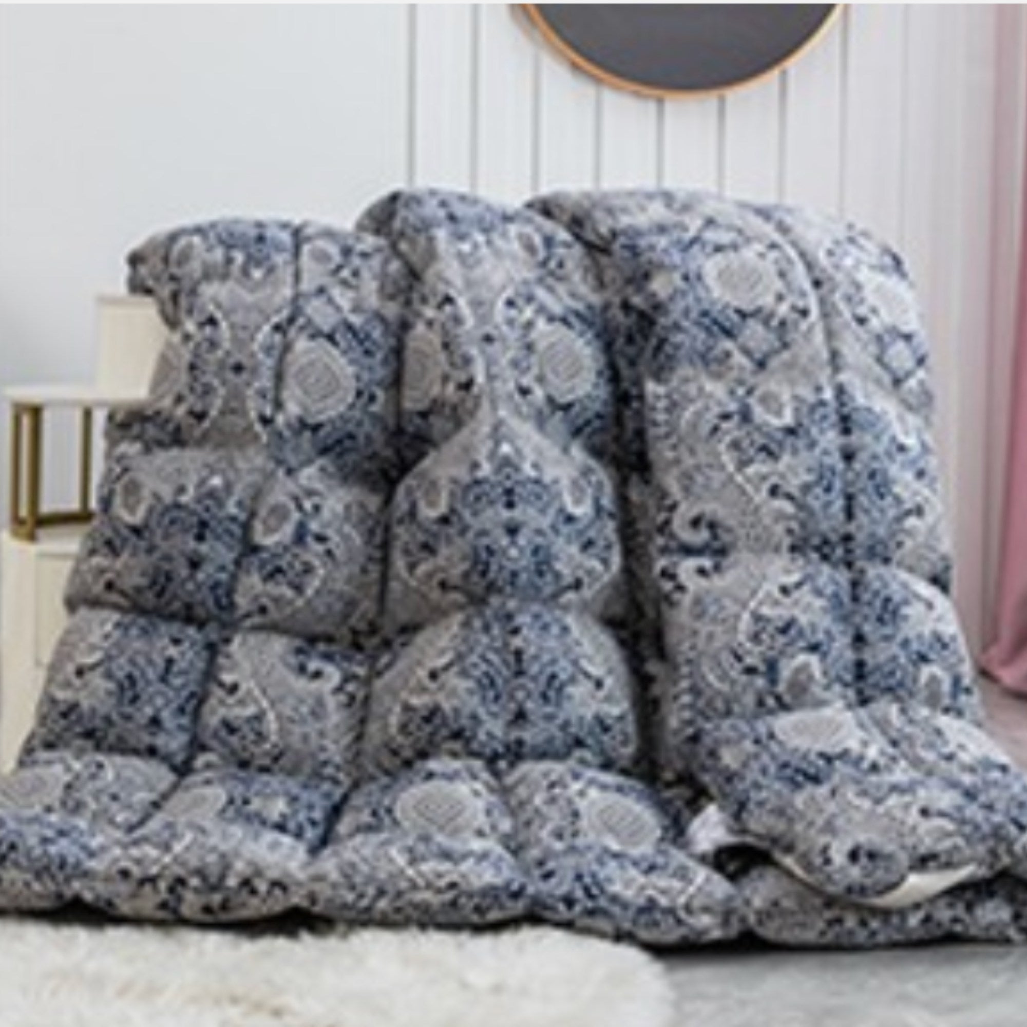 A thick, quilted comforter with a blue and gray floral pattern, draped over a bed in a bedroom setting.