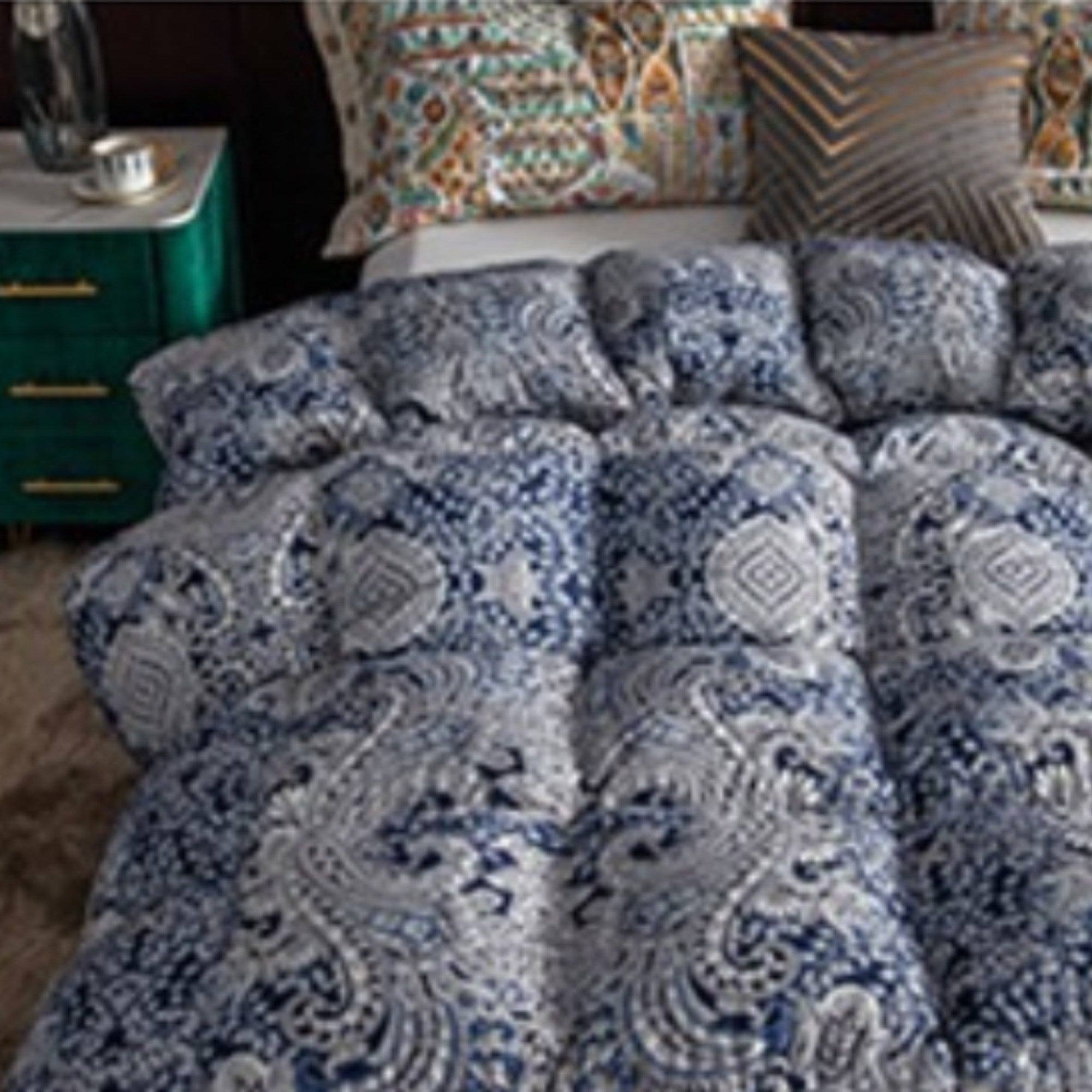 A close-up of a blue and white patterned comforter or duvet on a bed, with matching pillows and a green bedside table partially visible on the left.