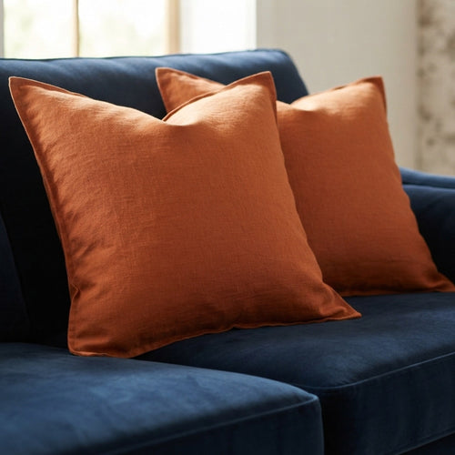 Two rust-orange throw pillows resting on a dark blue velvet sofa in a softly lit interior setting.
