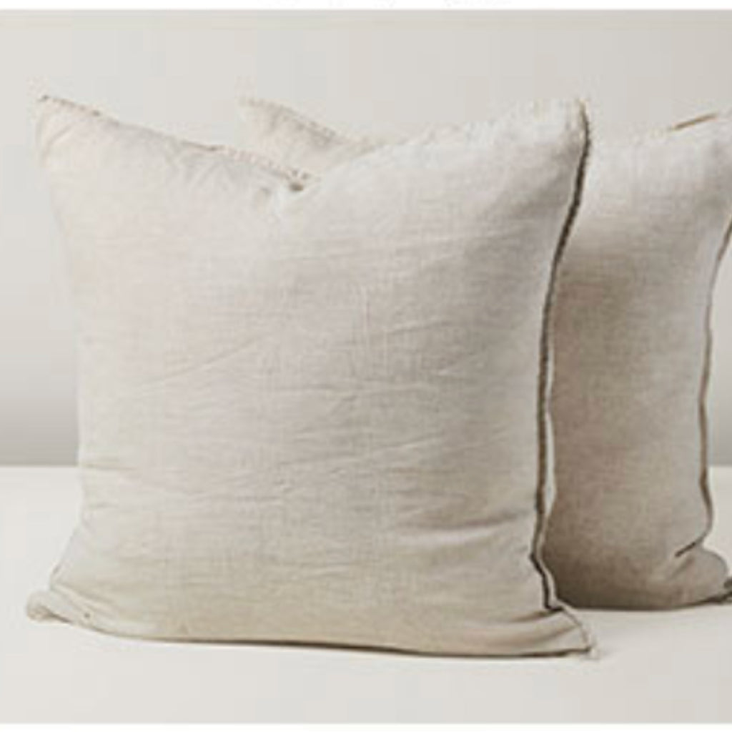 Two square linen pillows in a natural linen-like beige fabric, with the front pillow slightly overlapping the second one, set against a plain light background.
