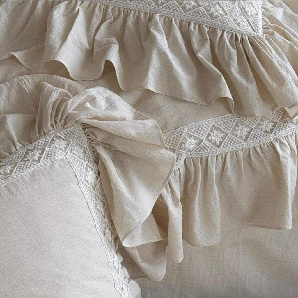 Close-up of a cream-colored ruffled fabric with delicate white embroidered detailing along the ruffles.