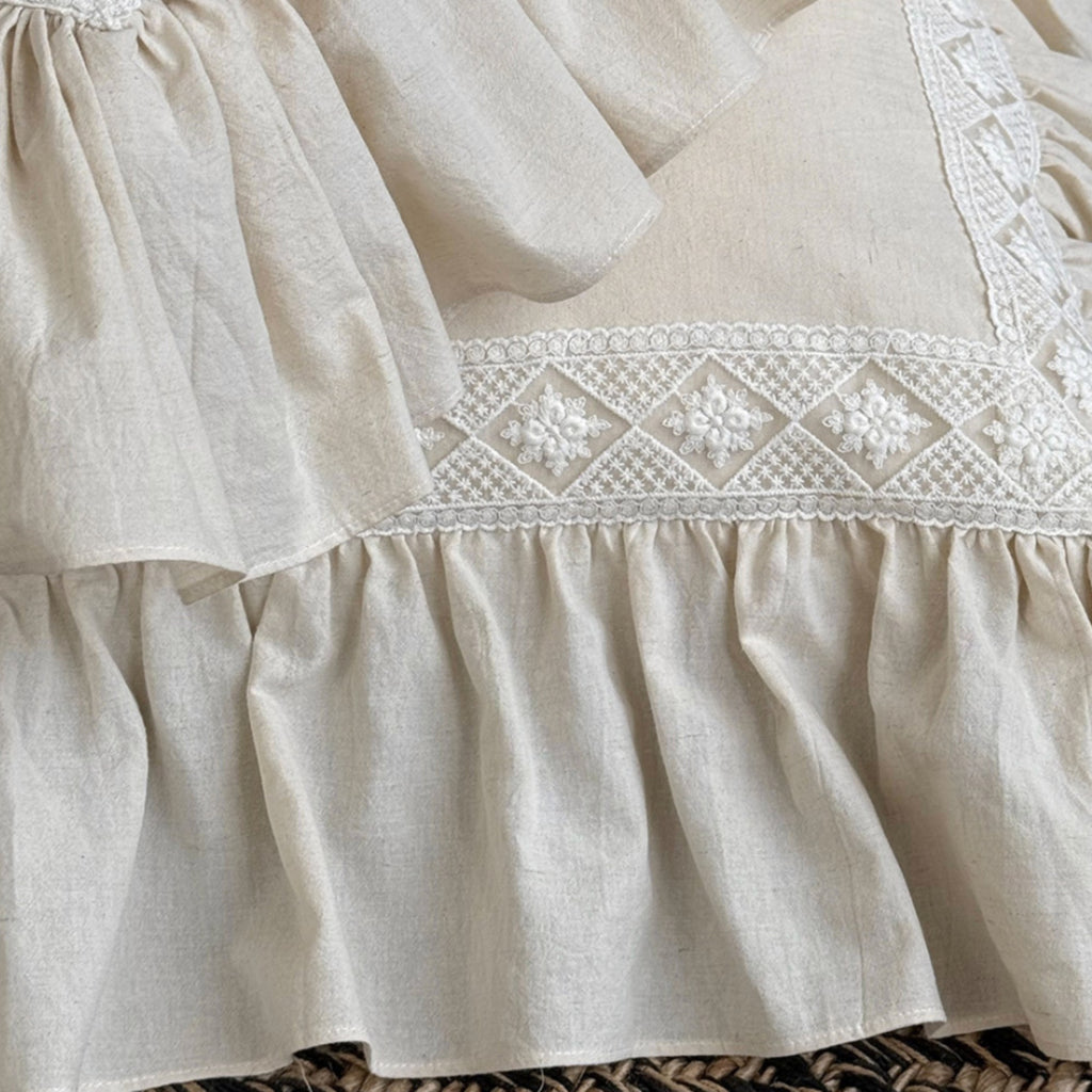 Close-up of a cream-colored linen dress or skirt with detailed white floral embroidery and a ruffled hem.