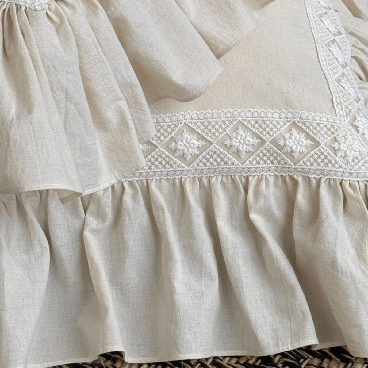 Close-up of a cream-colored linen dress or skirt with detailed white floral embroidery and a ruffled hem.