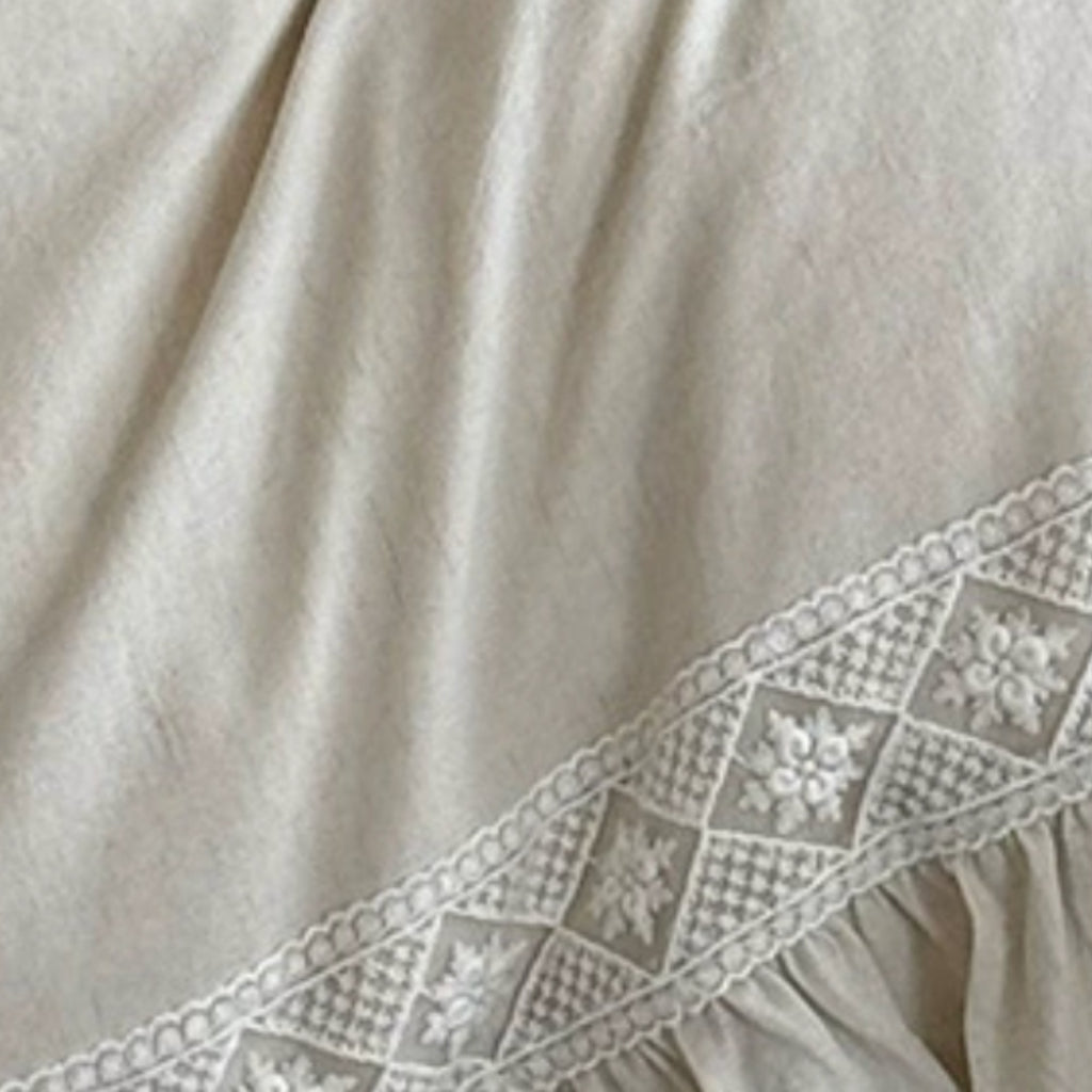 Close-up of a light beige fabric with a decorative embroidered lace border along the edge.