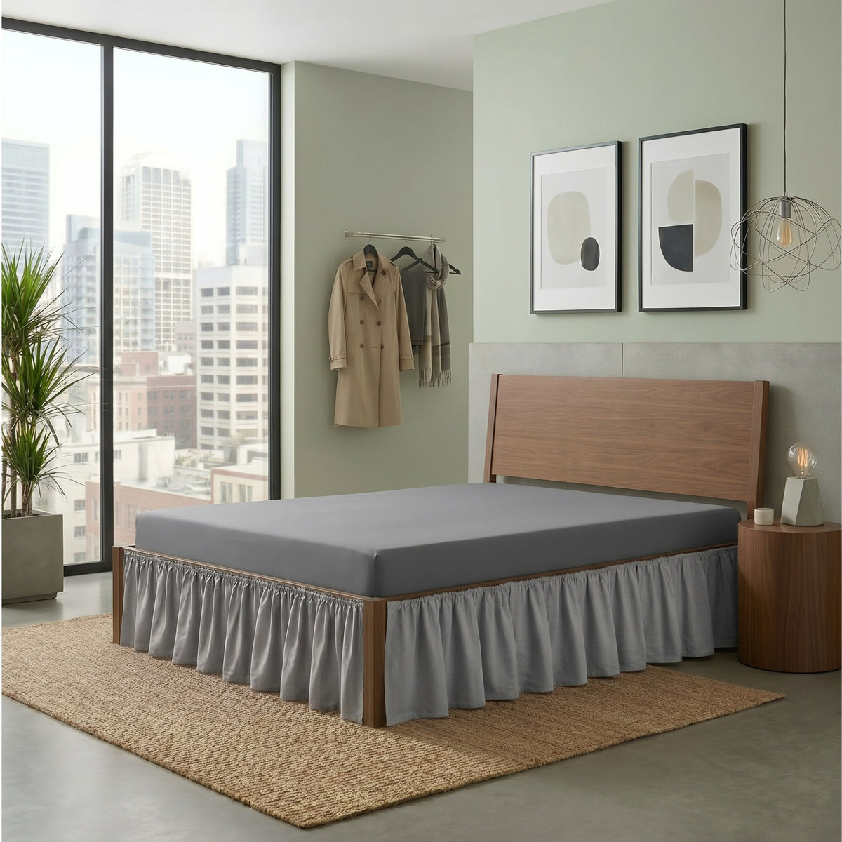 A modern bed frame with a gray ruffled skirt and gray mattress, shown in a styled bedroom setting with a city view, wall art, and a side table.