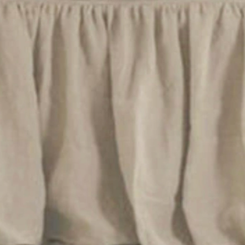 A close-up of a beige bed skirt with gathered pleats and a scalloped edge.