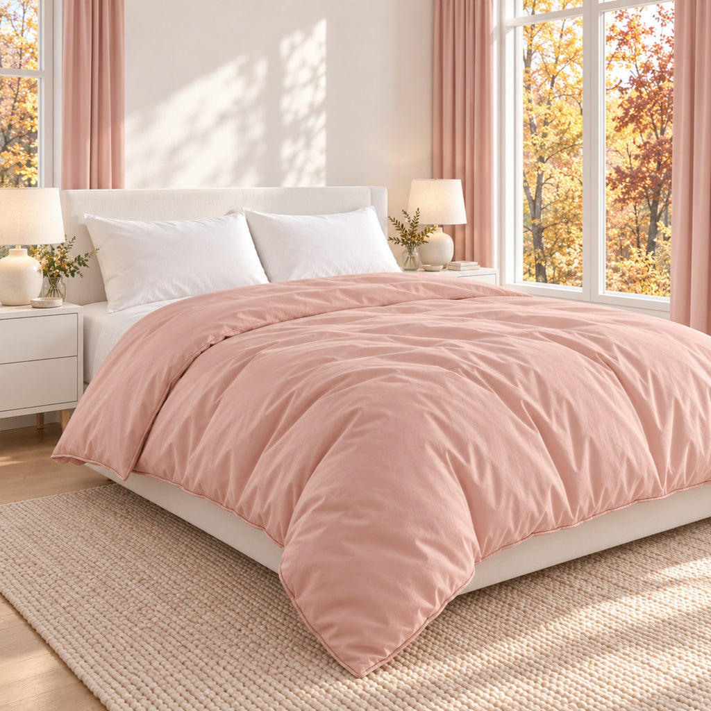 A blush pink  outer cover  filling 100% mulberry silk with matching pillowcases on a white bed in a bright, modern bedroom with pink curtains, white nightstands, and large windows showing autumn trees outside.