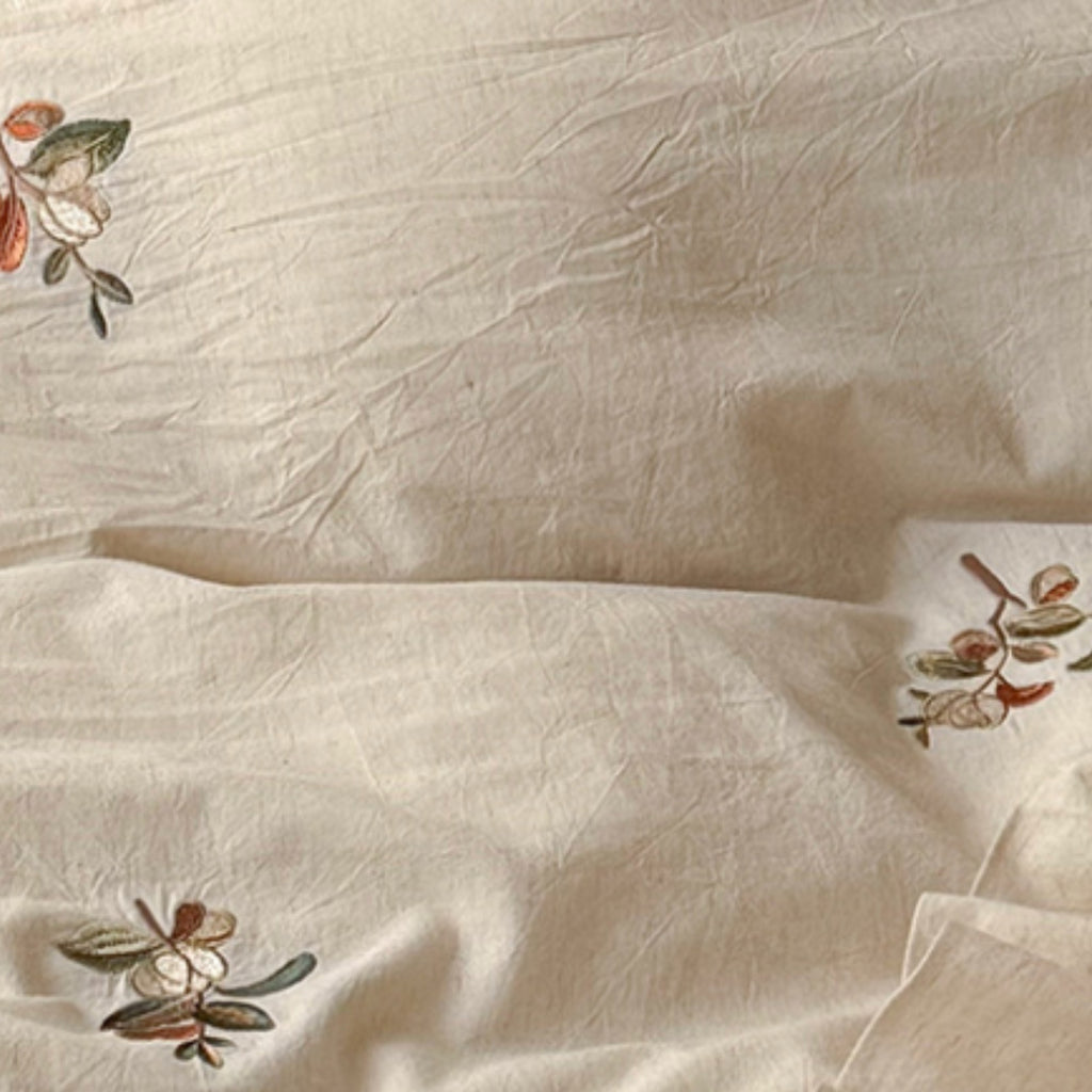Close-up of a cream-colored crinkled fabric with delicate embroidered floral motifs in muted green, brown, and orange tones.