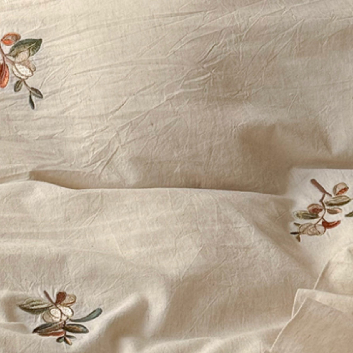 Close-up of a cream-colored crinkled fabric with delicate embroidered floral motifs in muted green, brown, and orange tones.